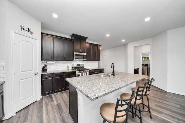 kitchen featuring wood finished floors, appliances with stainless steel finishes, backsplash, a sink, and washer and clothes dryer
