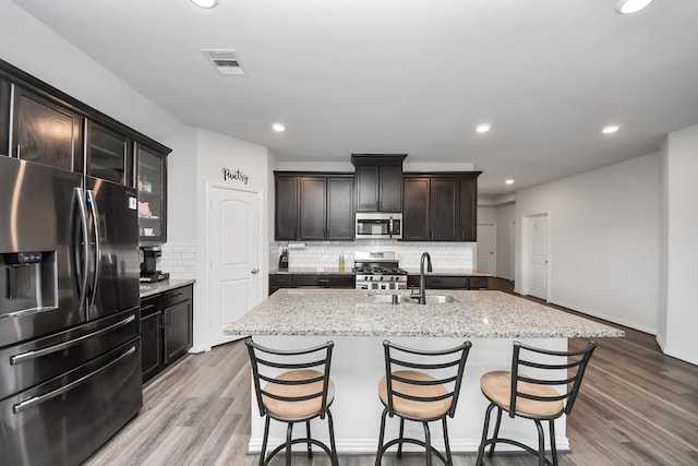 kitchen featuring sink, tasteful backsplash, dark brown cabinets, appliances with stainless steel finishes, and a kitchen island with sink