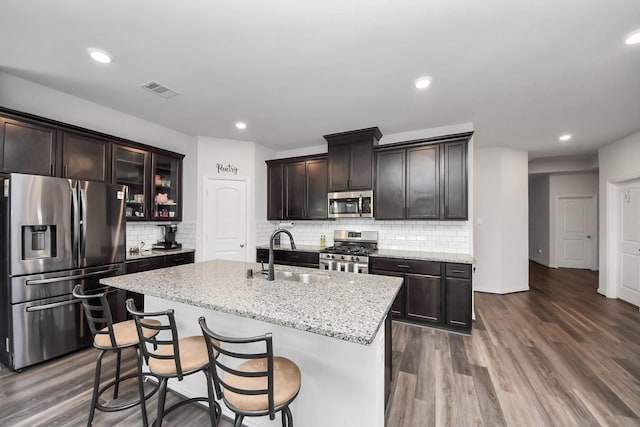 kitchen featuring stainless steel appliances, glass insert cabinets, a sink, and a center island with sink