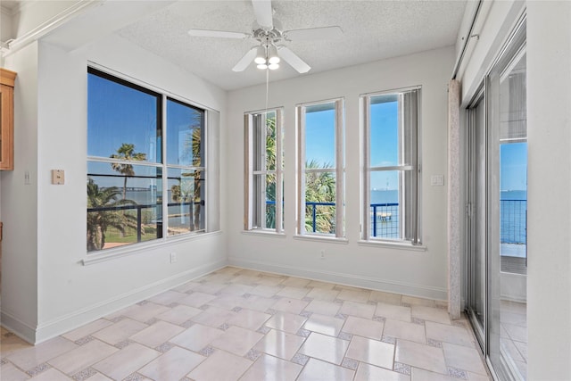 unfurnished sunroom with ceiling fan and a water view