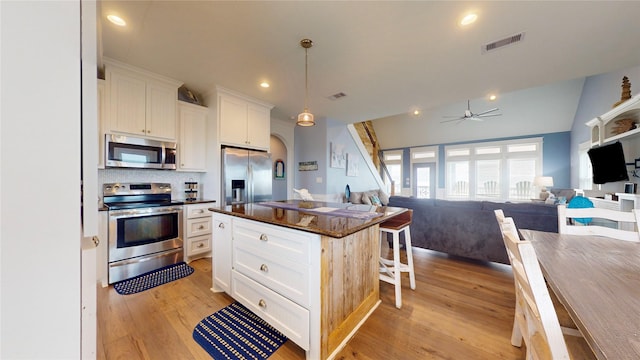 kitchen featuring appliances with stainless steel finishes, a kitchen island, decorative light fixtures, white cabinetry, and a breakfast bar