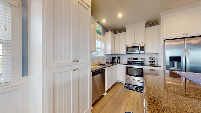 kitchen with dark stone countertops, light hardwood / wood-style floors, sink, white cabinetry, and appliances with stainless steel finishes