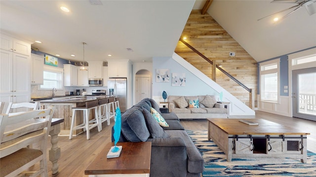 living room with ceiling fan, high vaulted ceiling, beam ceiling, light hardwood / wood-style flooring, and sink