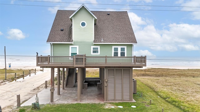 rear view of house with a patio area, a deck with water view, a yard, and a view of the beach