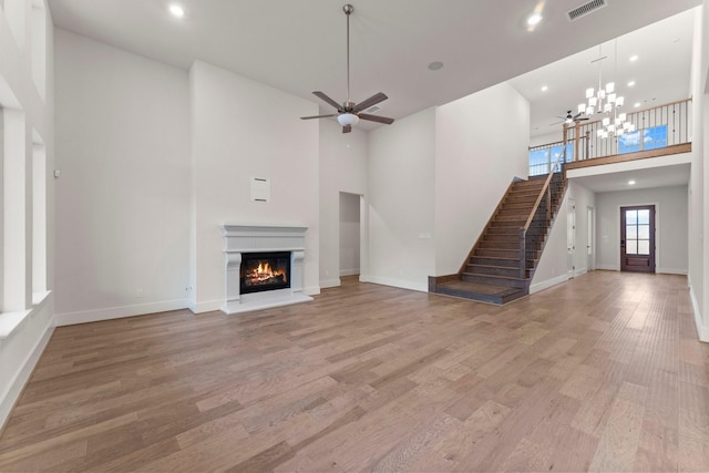 unfurnished living room featuring ceiling fan with notable chandelier, light hardwood / wood-style floors, and a high ceiling