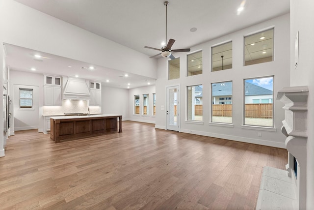 unfurnished living room featuring sink, light hardwood / wood-style flooring, ceiling fan, and a high ceiling