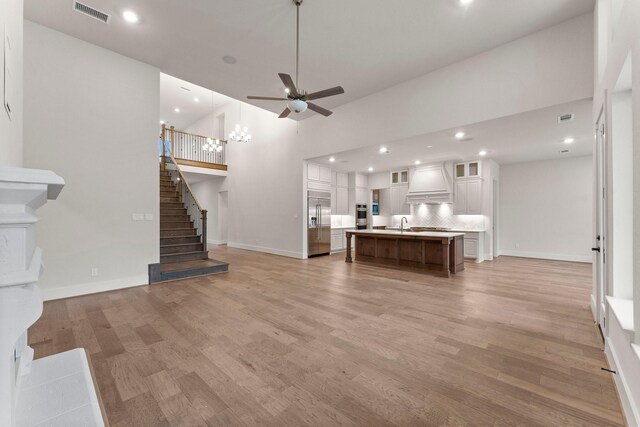 unfurnished living room featuring light wood finished floors, visible vents, a towering ceiling, stairway, and ceiling fan with notable chandelier