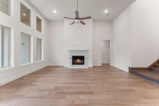 unfurnished living room with light hardwood / wood-style floors, ceiling fan, and a high ceiling