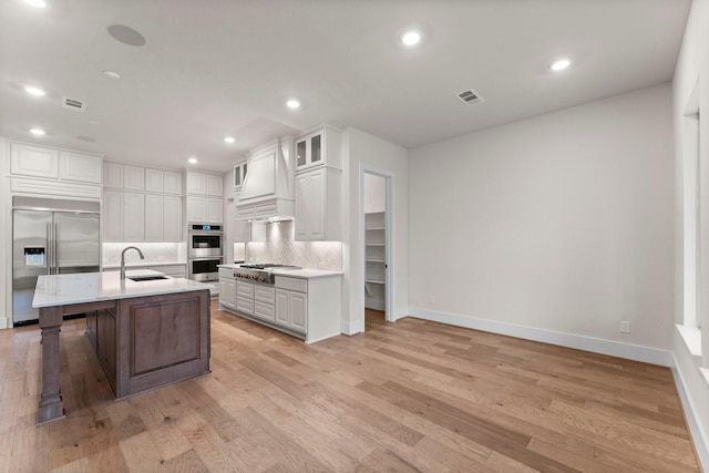 kitchen featuring sink, appliances with stainless steel finishes, white cabinetry, backsplash, and an island with sink