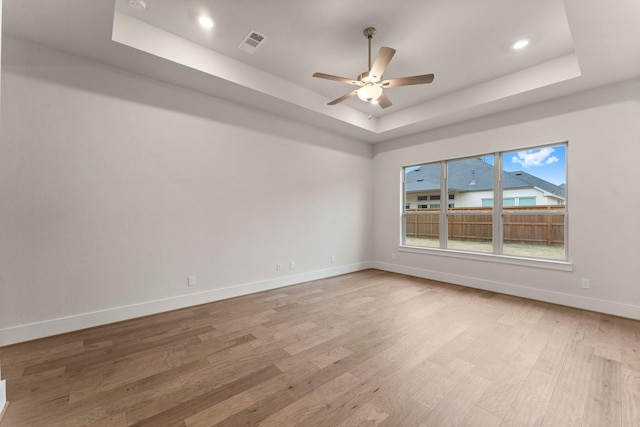 unfurnished room featuring baseboards, visible vents, ceiling fan, a tray ceiling, and light wood-style floors