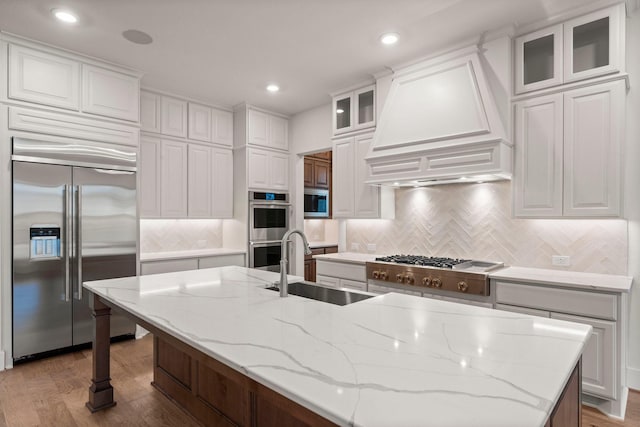 kitchen with stainless steel appliances, premium range hood, a sink, and white cabinets