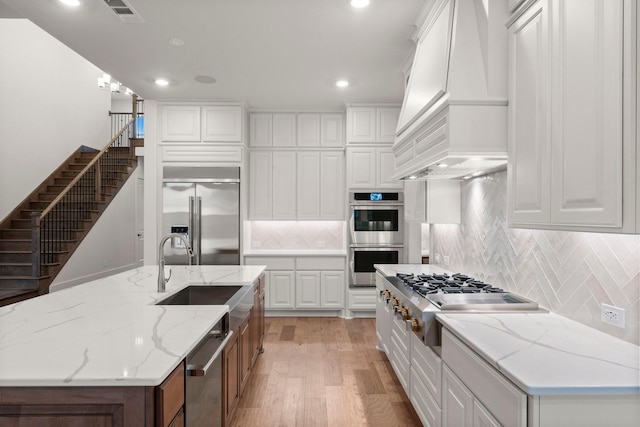 kitchen with stainless steel appliances, a spacious island, light stone counters, white cabinets, and custom exhaust hood