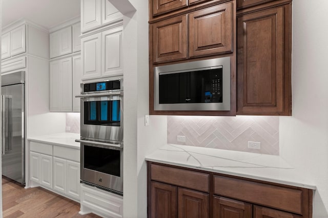 kitchen featuring white cabinetry, decorative backsplash, built in appliances, light stone counters, and light hardwood / wood-style flooring