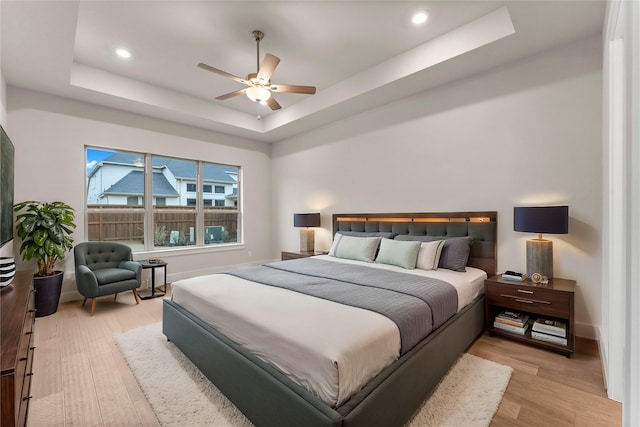 bedroom with a tray ceiling, light wood finished floors, recessed lighting, a ceiling fan, and baseboards