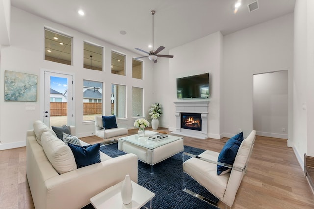 living room featuring a towering ceiling, light wood-style flooring, visible vents, and a glass covered fireplace