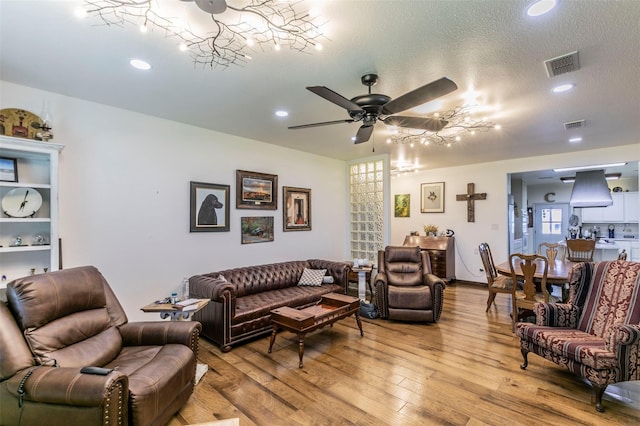 living room with ceiling fan with notable chandelier, a textured ceiling, and light hardwood / wood-style floors