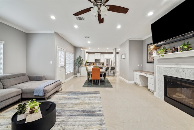 living room with ceiling fan, a tile fireplace, and crown molding