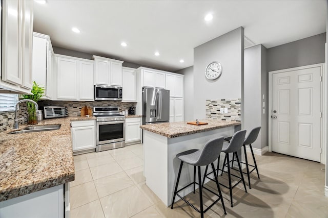 kitchen with white cabinetry, a breakfast bar area, stainless steel appliances, light stone counters, and sink