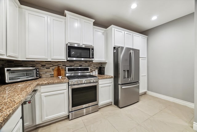 kitchen with light stone countertops, decorative backsplash, appliances with stainless steel finishes, and white cabinetry