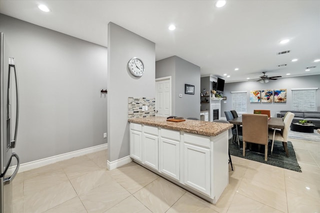 kitchen featuring white cabinets, decorative backsplash, stainless steel fridge with ice dispenser, ceiling fan, and light stone counters