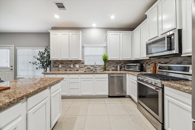 kitchen with white cabinetry, stainless steel appliances, tasteful backsplash, sink, and light stone counters