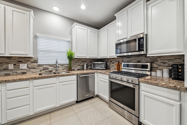 kitchen featuring white cabinets, appliances with stainless steel finishes, decorative backsplash, sink, and light tile patterned floors