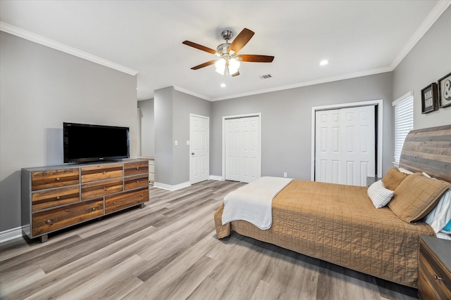 bedroom with ceiling fan, ornamental molding, two closets, and hardwood / wood-style flooring