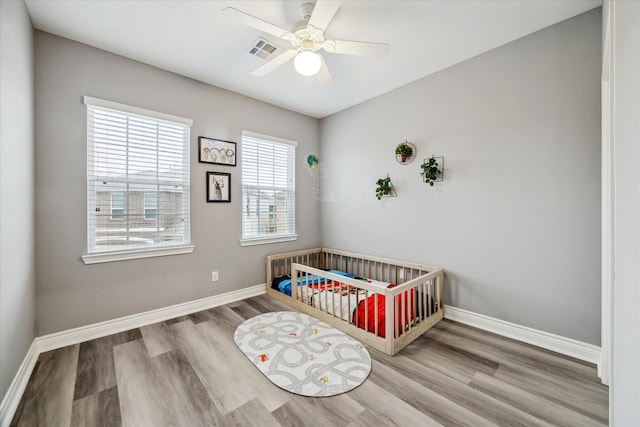 bedroom featuring ceiling fan, a crib, and hardwood / wood-style floors