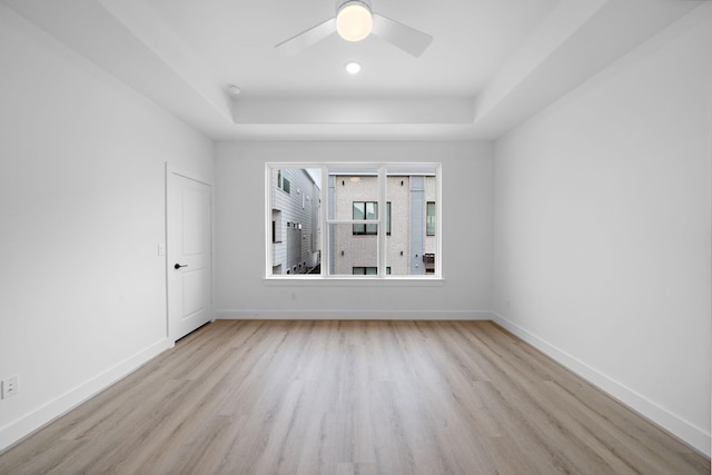 empty room with ceiling fan, light hardwood / wood-style floors, and a tray ceiling