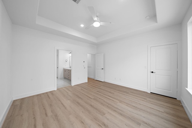 unfurnished bedroom featuring ceiling fan, light hardwood / wood-style floors, a tray ceiling, and ensuite bathroom