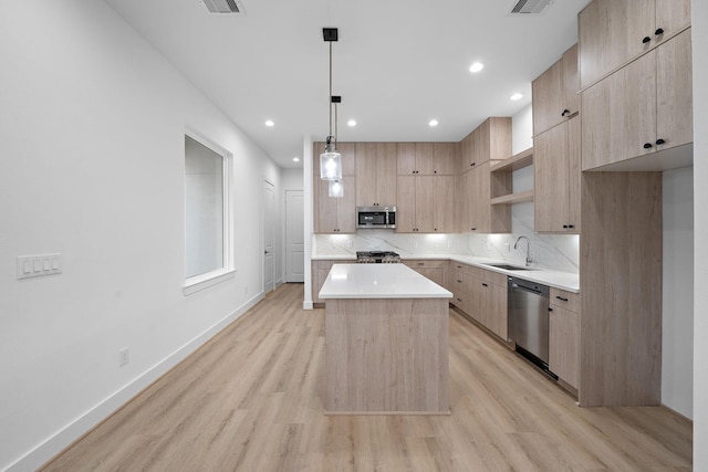 kitchen featuring appliances with stainless steel finishes, decorative light fixtures, light brown cabinetry, a kitchen island, and sink