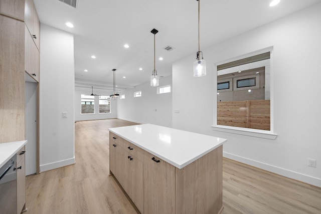 kitchen with light wood-type flooring, light brown cabinetry, hanging light fixtures, stainless steel dishwasher, and a center island