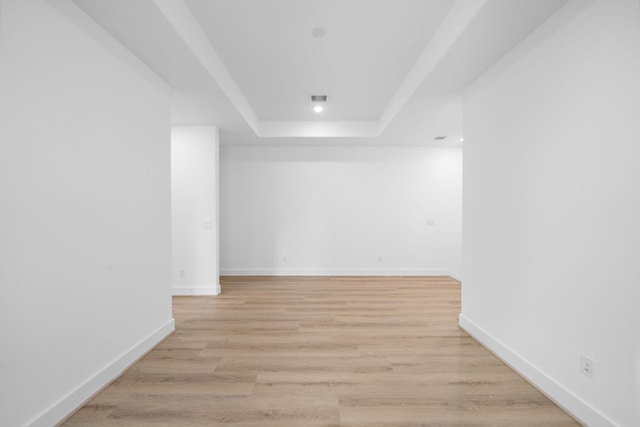 empty room with light wood-type flooring and a tray ceiling