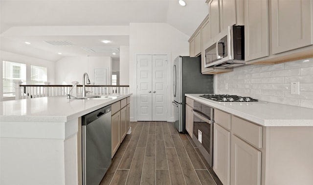 kitchen featuring lofted ceiling, a sink, stainless steel appliances, wood finish floors, and backsplash