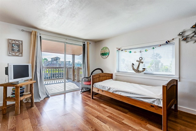 bedroom with wood-type flooring, access to outside, and a textured ceiling