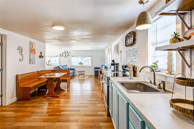 kitchen with light hardwood / wood-style floors, electric range, decorative light fixtures, a textured ceiling, and sink