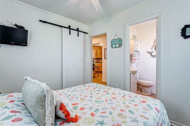 bedroom with ensuite bathroom, a barn door, ceiling fan, and ornamental molding