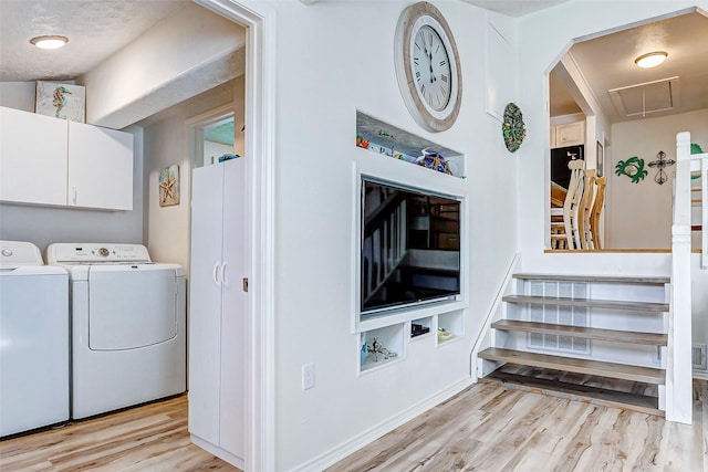 clothes washing area with washer and clothes dryer, a textured ceiling, light hardwood / wood-style floors, and cabinets