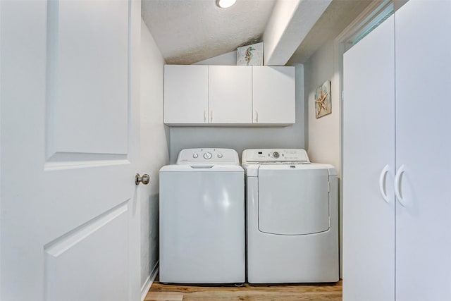 laundry room featuring a textured ceiling, separate washer and dryer, cabinets, and light wood-type flooring