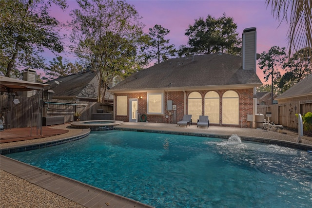 pool at dusk featuring an in ground hot tub