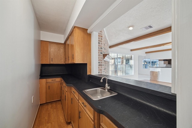 kitchen with beamed ceiling, sink, a textured ceiling, and light hardwood / wood-style floors