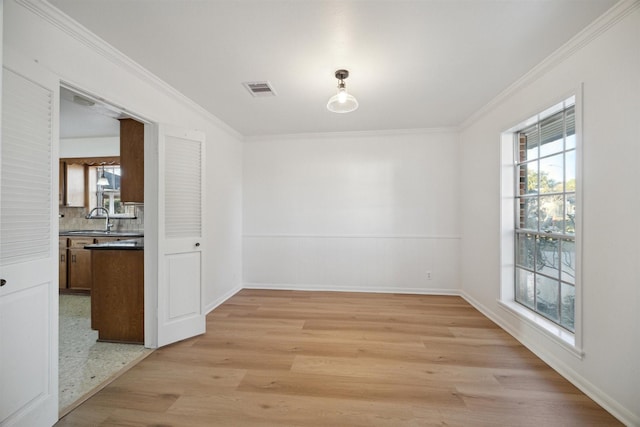 unfurnished dining area featuring ornamental molding, sink, and light wood-type flooring