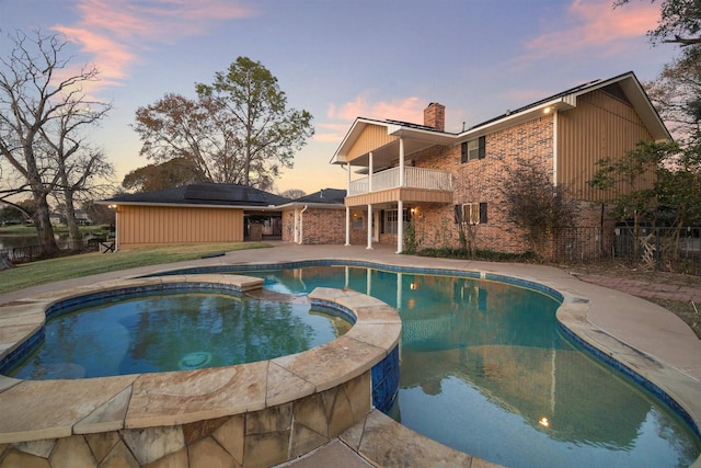 pool at dusk featuring an in ground hot tub