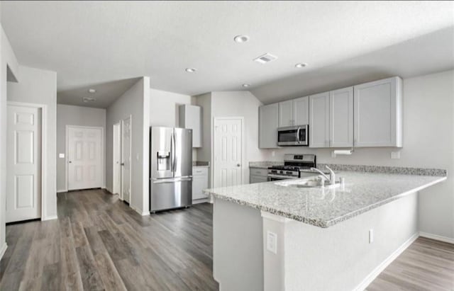 kitchen featuring kitchen peninsula, appliances with stainless steel finishes, light stone countertops, white cabinets, and sink