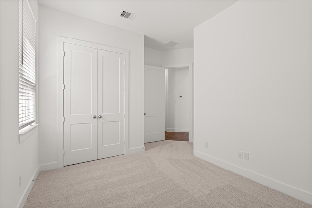 unfurnished bedroom with light colored carpet and a closet