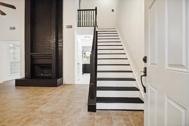 stairway featuring a brick fireplace, a towering ceiling, and tile patterned flooring