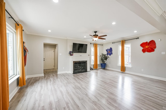 unfurnished living room with a tiled fireplace, a wealth of natural light, crown molding, and light hardwood / wood-style flooring