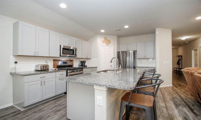 kitchen with white cabinets, appliances with stainless steel finishes, a kitchen bar, an island with sink, and sink