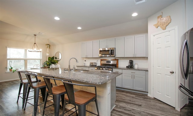 kitchen featuring decorative light fixtures, sink, a kitchen island with sink, appliances with stainless steel finishes, and white cabinets