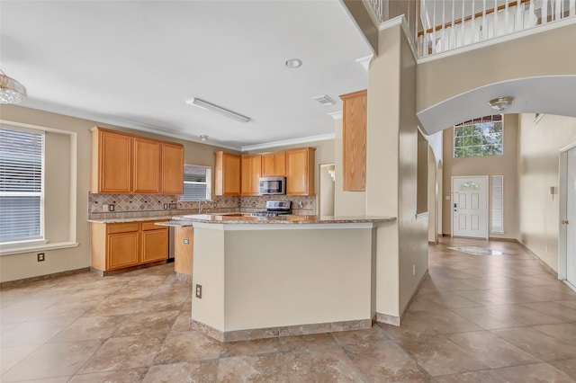 kitchen featuring kitchen peninsula, appliances with stainless steel finishes, backsplash, light stone countertops, and crown molding